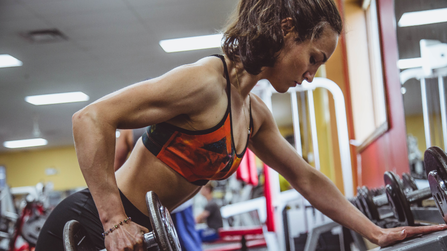 Frau trainiert Rücken mit Kurzhantel im Fitnessstudio.