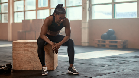 Fit woman resting on plyo box during gym workout.
