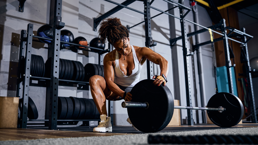 Femme musclée ajustant une barre de musculation en salle.