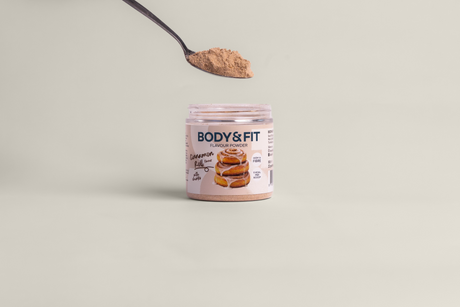 Pot de Flavour Powder Body&Fit, parfum Cinnamon Roll, avec une cuillère de poudre au-dessus, étiquette indiquant "Rich in Fibre" et "11 kcal per scoop".