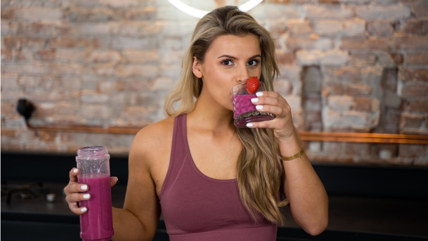 Vrouw drinkt roze smoothie met aardbei in sportkeuken.