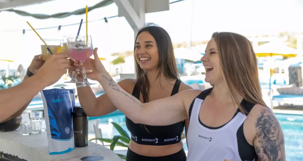 Women in sportswear cheering with drinks by the pool.