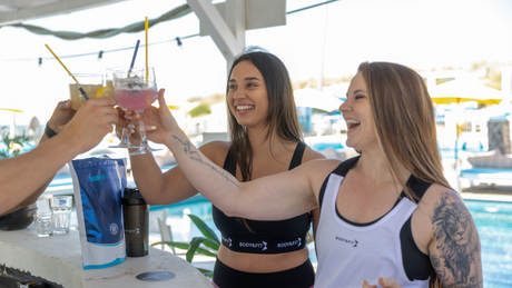 Drei Frauen stoßen mit Cocktails an beim Outdoor-Fitness-Event.