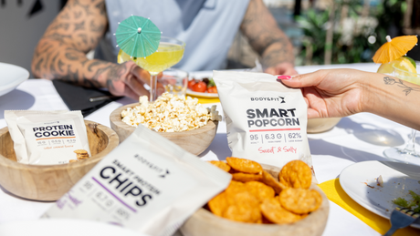Proteinreiche Snacks wie Popcorn, Chips und Cookies auf Tisch.