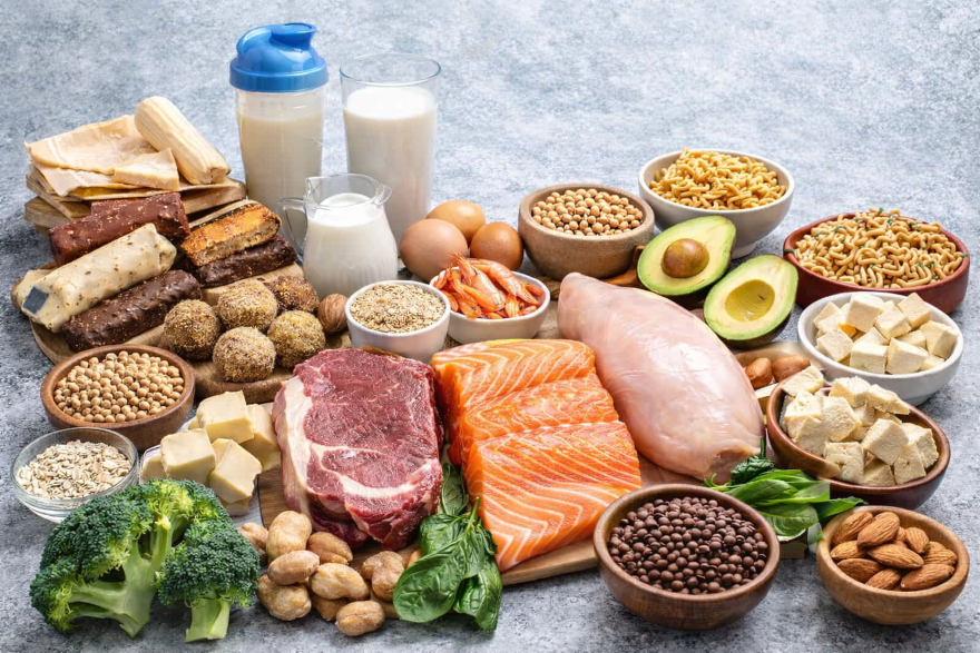 Verschiedene proteinreiche Lebensmittel wie Fleisch, Fisch, Eier, Milchprodukte, Hülsenfrüchte und ein Proteinshake