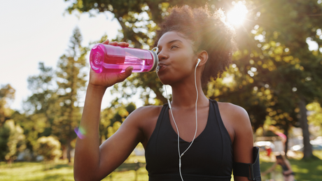 Frau trinkt Wasser aus pinker Flasche beim Outdoor-Training.