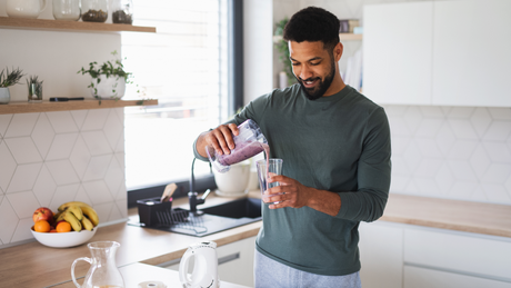 Man pouring berry smoothie into glass in modern kitchen.