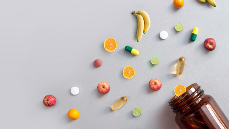 Scattered vitamins and fruit slices with open supplement bottle.