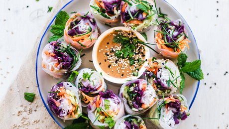 Fresh vegetable spring rolls with dipping sauce on a white plate.