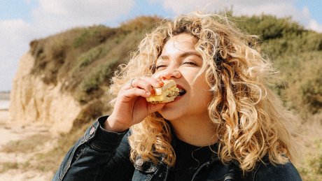 Woman eating sandwich outdoors with windblown curly hair.