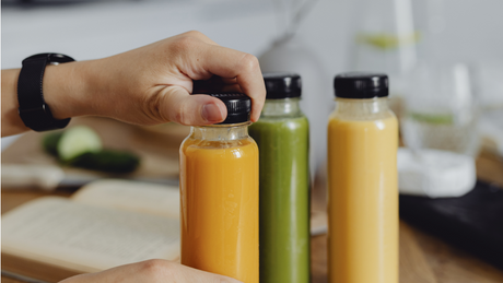 Hand holding bottle of orange juice beside green and yellow juices.