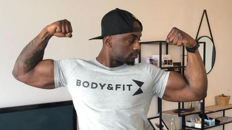 Man toont spierballen in grijs Body&Fit shirt.