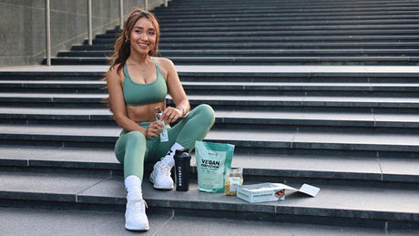 Vrouw in sportoutfit met vegan eiwitrepen en supplementen.