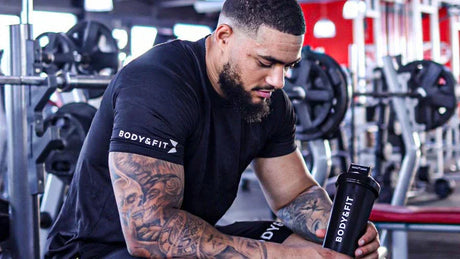 Tätowierter Mann macht Pause im Fitnessstudio mit einem Body&Fit Shaker.