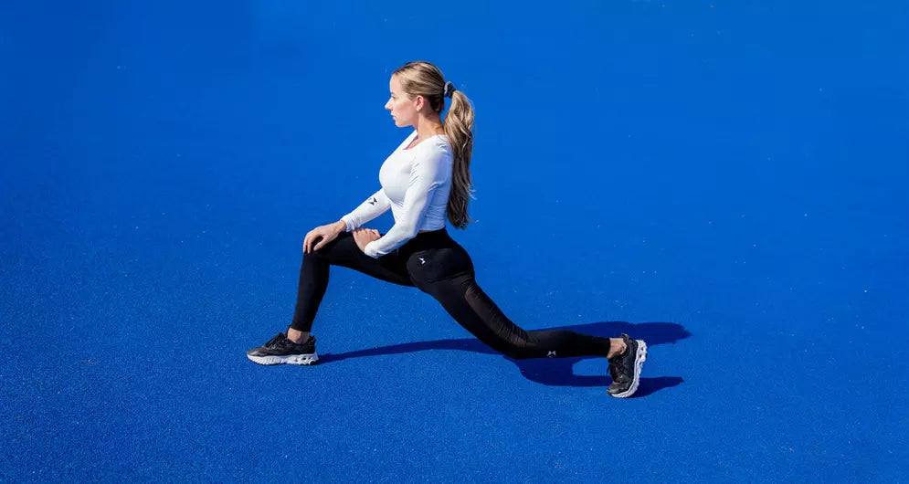 Sportlerin macht Ausfallschritt-Stretching auf blauem Outdoor-Sportboden.