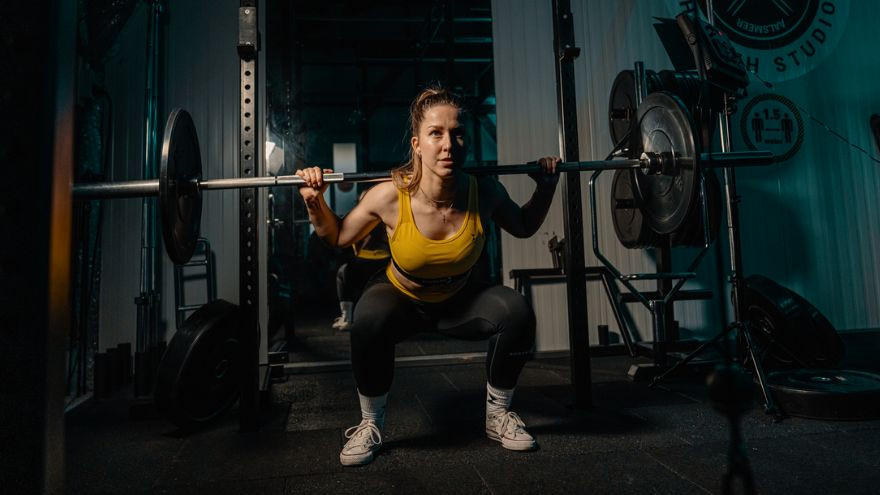 Femme en squat avec barre de musculation en salle.