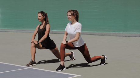 Two women doing forward lunges on tennis court.
