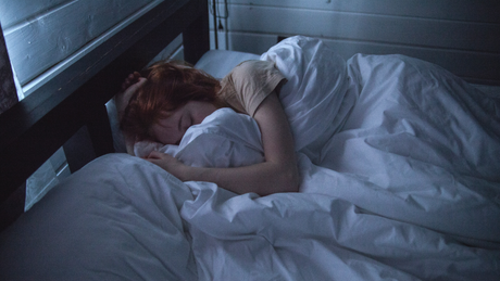 Femme endormie dans un lit sous une couette blanche.