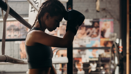 Female boxer resting in ring with gloves on forehead.