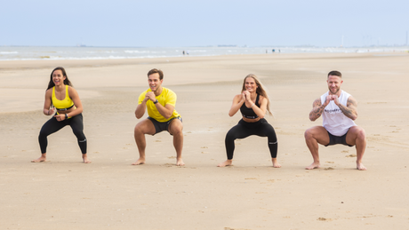 Group doing squats on sandy beach during outdoor workout.
