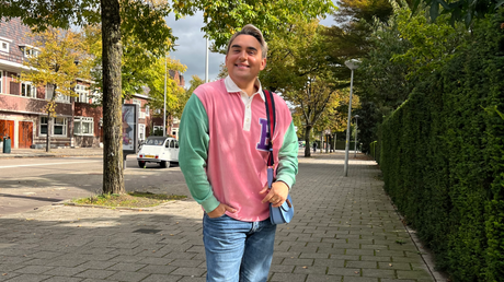 Smiling man in colorful shirt walking on city sidewalk.