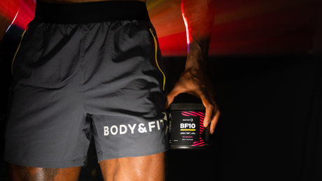 Mann hält Body&Fit-Pre-Workout in Hand mit dynamischem Lichteffekt.