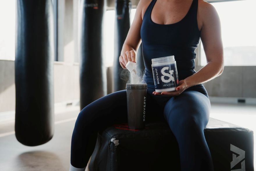 Frau gibt einen Messlöffel Perfection Pre-Workout in einen Body&Fit Shaker im Gym