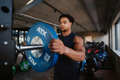 Man loading a 20kg weight plate onto a barbell in the gym