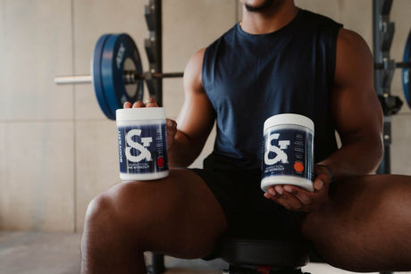 Athlete in the gym holding two tubs of Perfection Pre-Workout in Red Energy and Fruit Punch flavours