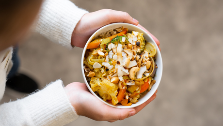 Kom met groentecurry, noten en kokosvlokken in handen gehouden.