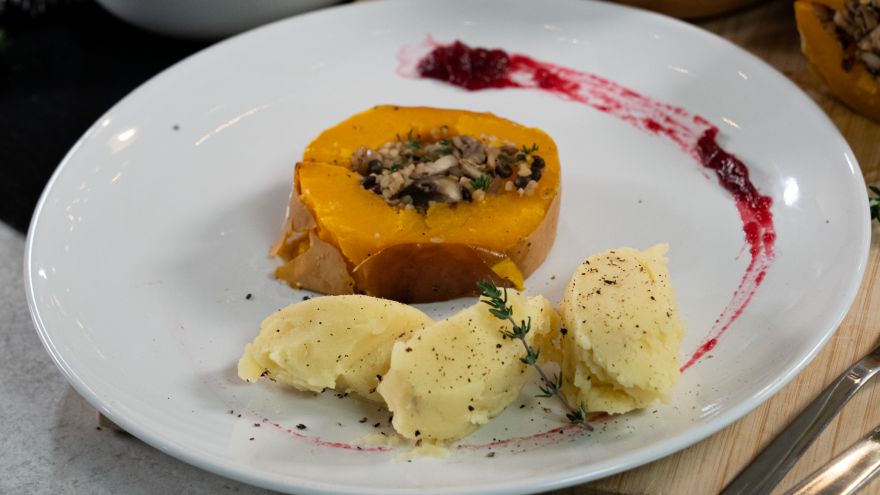 Pompoen gevuld met linzenmix en aardappelpuree op bord.