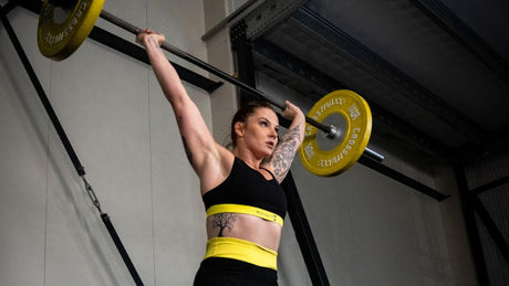 Female athlete performing overhead barbell lift.