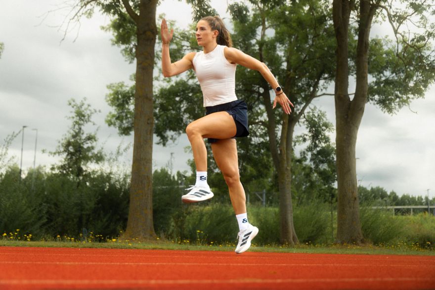 Vrouw sprint op een atletiekbaan buiten, knie opgetrokken tijdens het hardlopen, met een goede looptechniek
