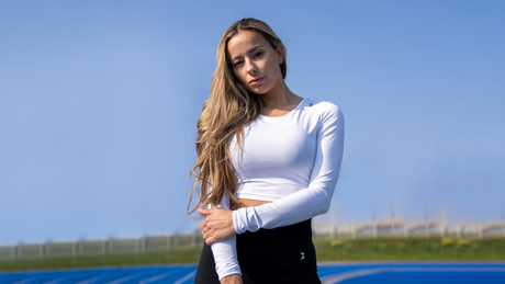 Junge Frau in weißem Sporttop posiert auf Laufbahn.