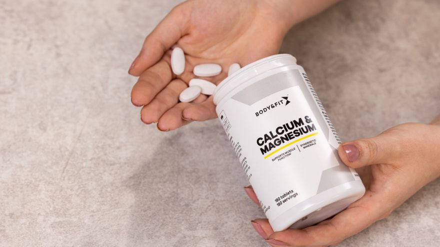 Handen houden calcium- en magnesiumsupplementen van Body&Fit vast.