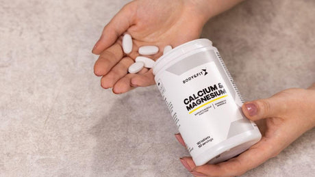 Handen houden calcium- en magnesiumsupplementen van Body&Fit vast.