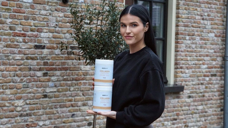 Woman holding Body&Fit collagen protein drink containers outdoors.