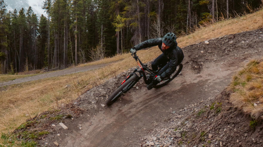 Mountainbiker rijdt scherpe bocht op modderig bospad.