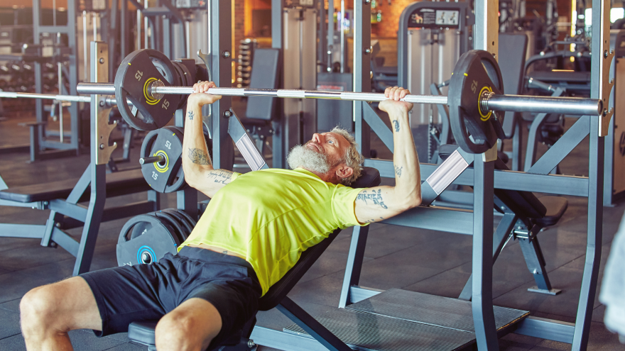 Oudere man doet bankdrukken in moderne sportschool.