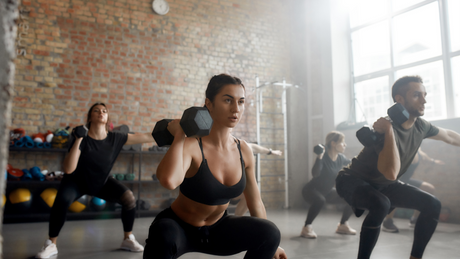 Groep mensen doet squats met gewichten in sportschool.