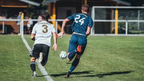 Two soccer players chasing ball on grassy field.