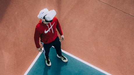 Homme en sweat rouge avec casque VR sur terrain de sport.