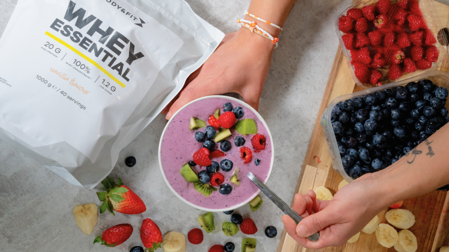Smoothie Bowl mit Beeren und Kiwi neben Whey Essential Proteinpulver.