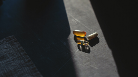 Assorted vitamin and omega capsules on dark surface in natural light.