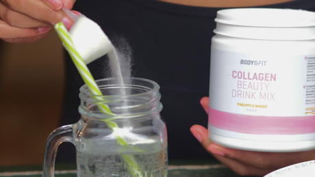Pouring collagen drink mix into glass jar with straw.