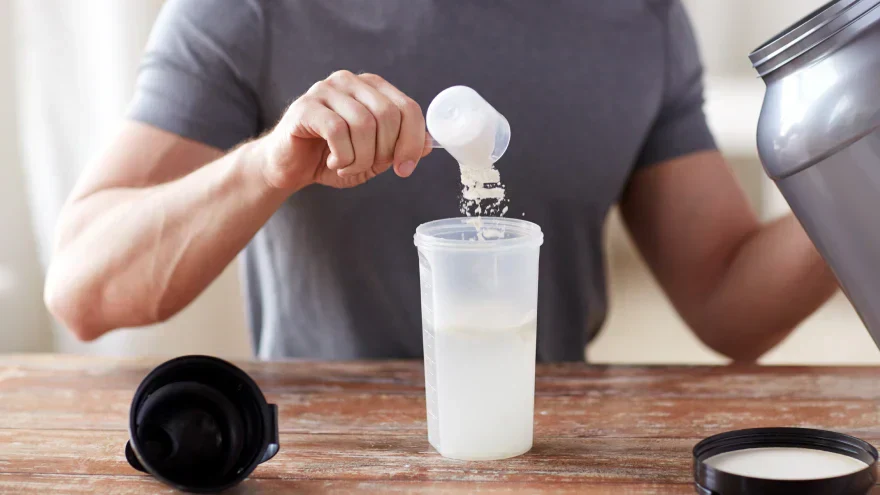 Scooping protein powder into a shaker for post-workout nutrition.
