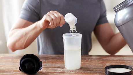 Scooping protein powder into a shaker for post-workout nutrition.