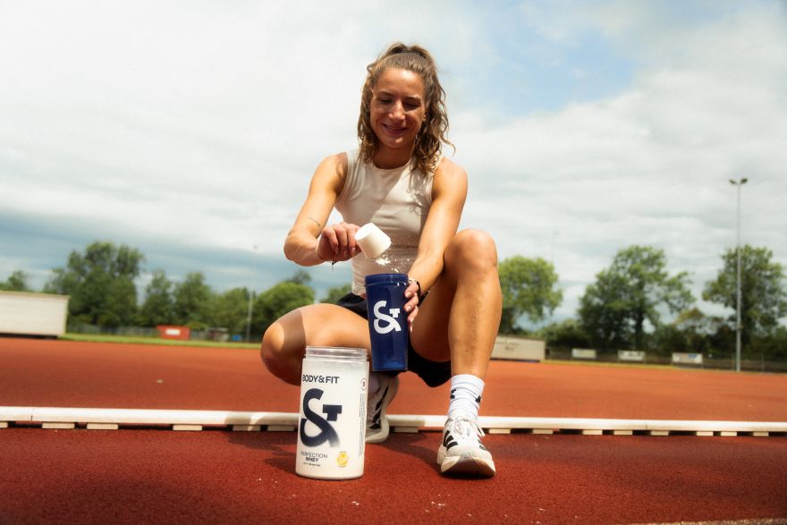 Frau auf einer Laufbahn füllt Body&Fit Perfection Whey Proteinpulver in einen Shaker