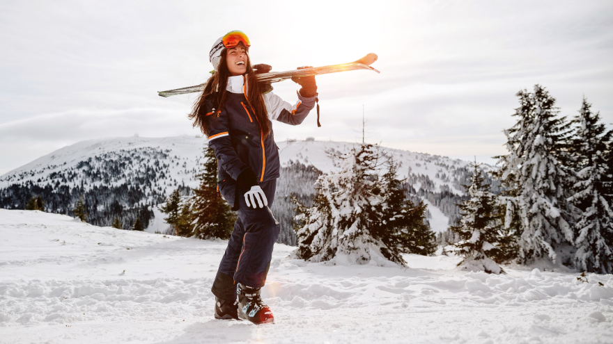 Smiling woman carrying skis in winter mountain landscape.