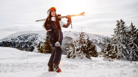 Smiling woman carrying skis in winter mountain landscape.